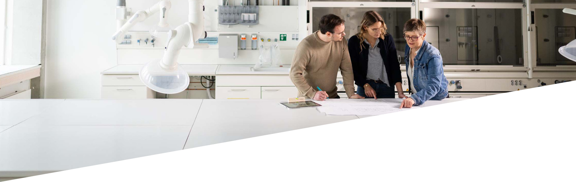 Drei GMSH-Mitarbeiter prüfen einen Grundriss. Sie sind in einem neu gebauten Laborraum.