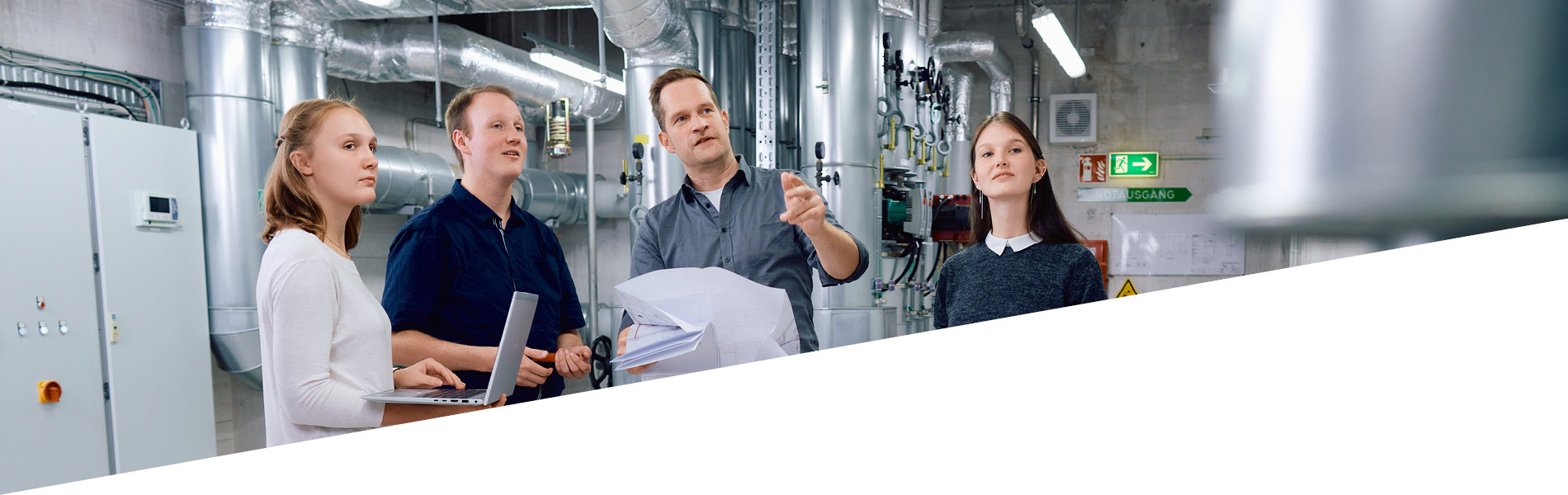GMSH-Ausbilder zeigt drei GMSH-Azubis eine technische Anlage.